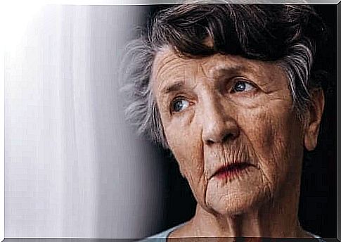 An elderly woman stands next to the window