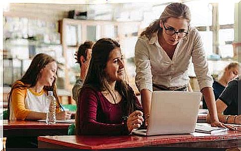 A student sits behind her laptop while a teacher watches her